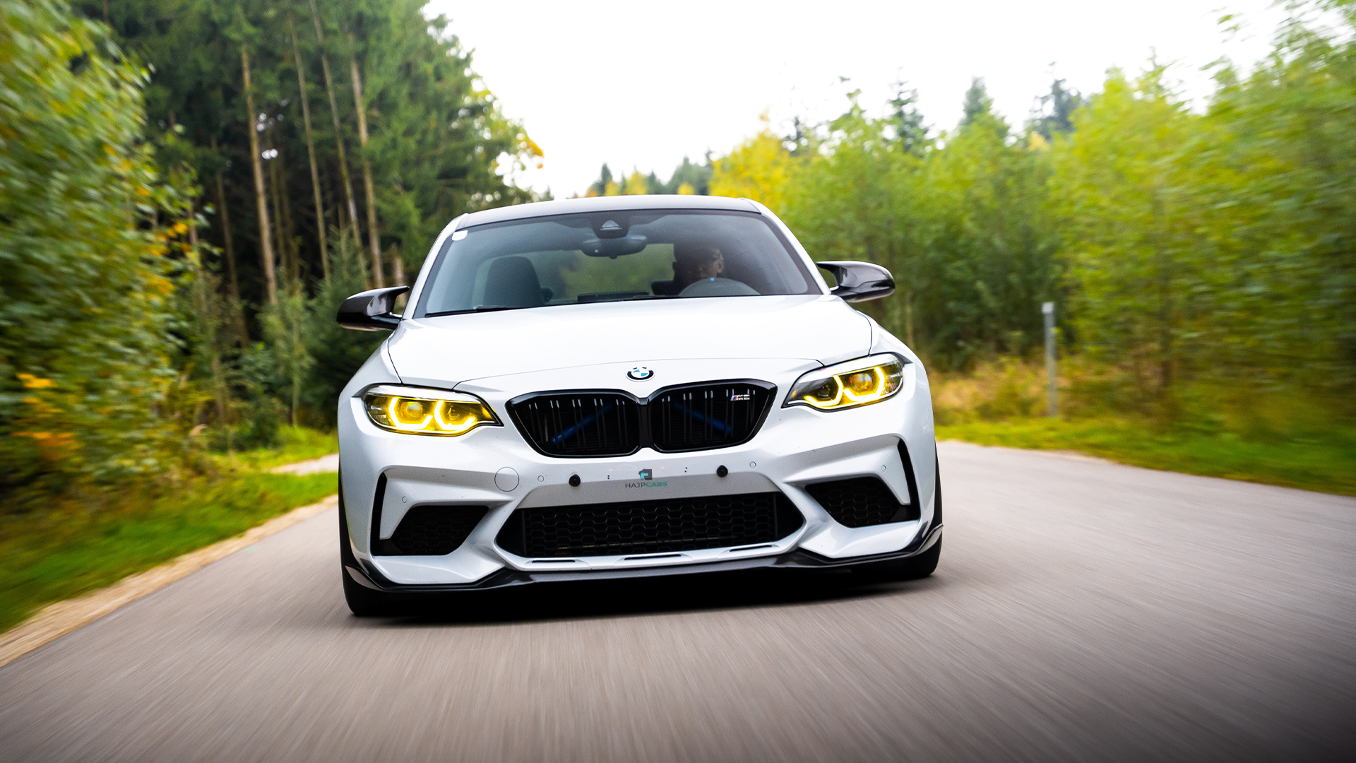 BMW M2 rolling shot through green forest with yellow drl's